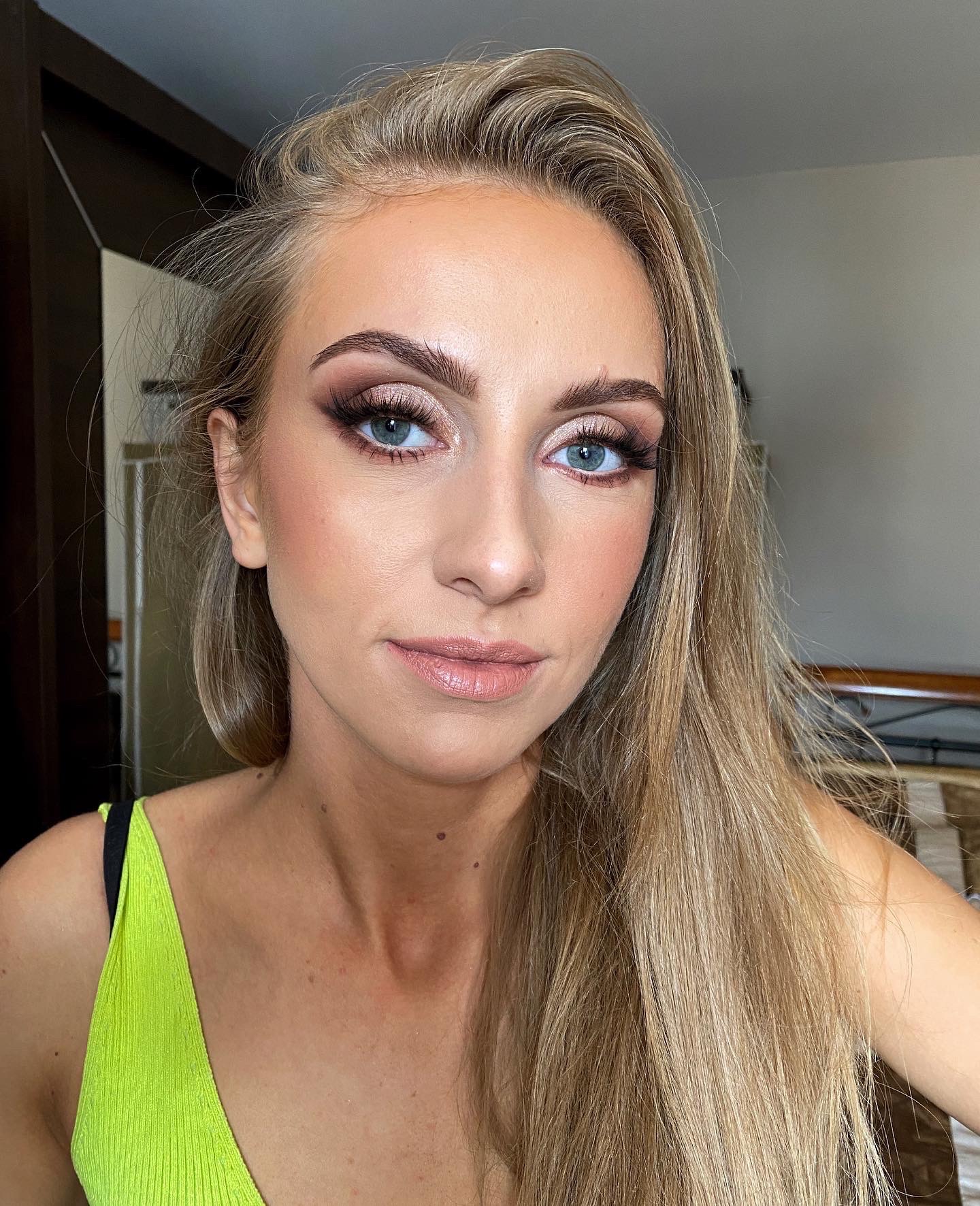 Portret blondynki z delikatnym, rozświetlonym makijażem oczu w odcieniach brązu i beżu, z wyraźnie podkreślonymi rzęsami i brwiami, oraz subtelnym konturowaniem twarzy i ustami w odcieniu nude.