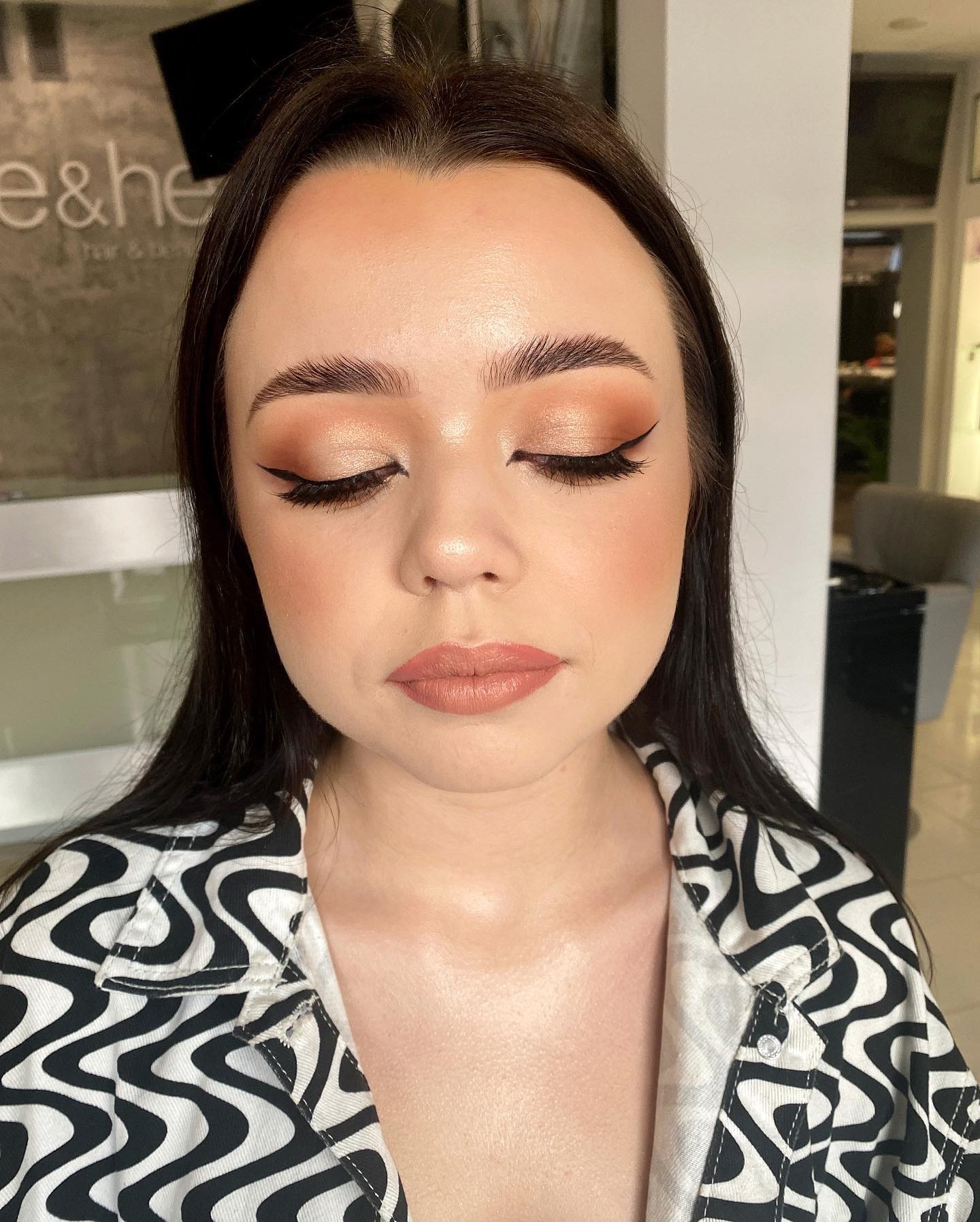 Portret kobiety z zamkniętymi oczami prezentujący wykonany w Kielcach dzienny makijaż z kreską eyelinerem, brązowymi cieniami i pomadką w odcieniu nude, w tle salon kosmetyczny.