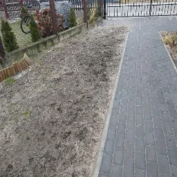 Przygotowany teren pod przyszły trawnik z widocznym fragmentem ułożonej kostki brukowej i bramą wjazdową.