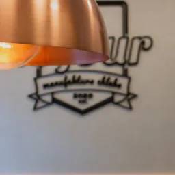 Miedziana lampa wisząca nad ścianą z logo piekarni 'Your manufaktura chleba 2020'.