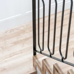 Nowoczesne schody z drewnianymi stopniami i czarną, metalową balustradą o minimalistycznym designie, widoczne z góry.
