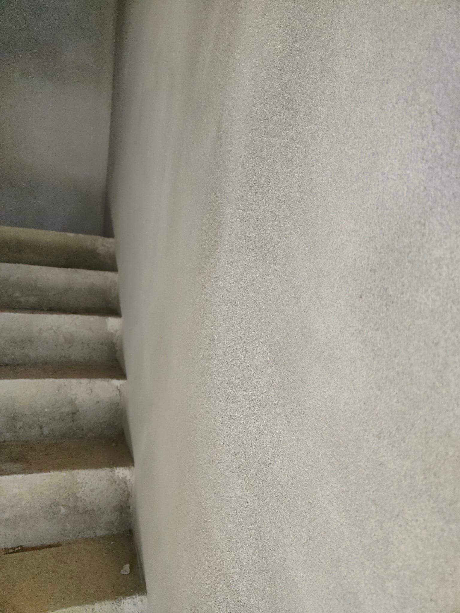 Surowe, betonowe schody wewnętrzne w trakcie prac wykończeniowych, z widoczną świeżo położoną szpachlą na ścianie obok, ukazując stan przed malowaniem.