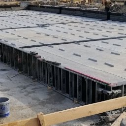 WD KONSTRUKCJE SP. Z O.O. - Szary fundament z deskowaniem i widocznymi elementami zbrojenia, przygotowany do zalania betonem, z pracownikami w tle.