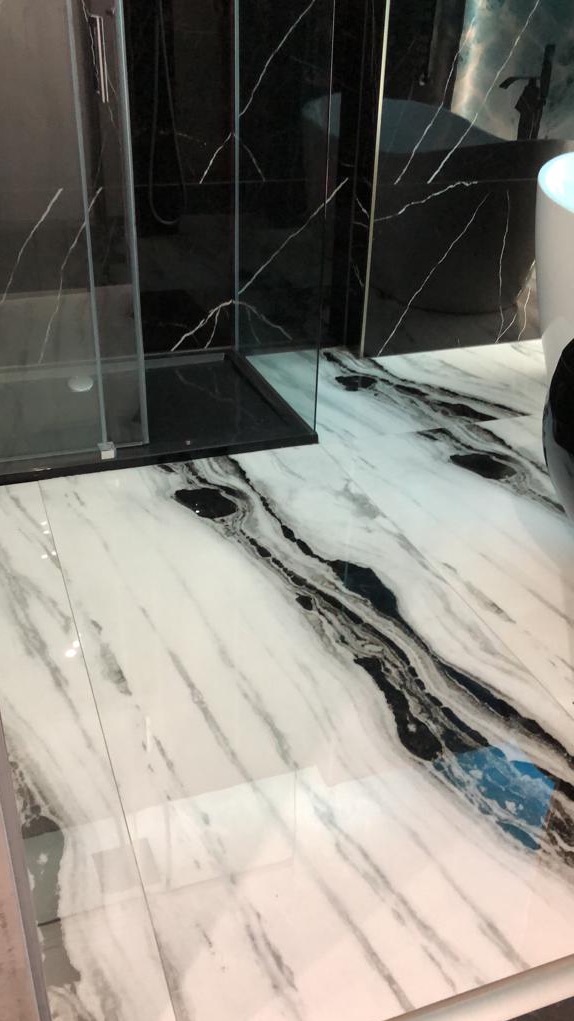 Biała marmurowa podłoga z czarnymi żyłami w łazience z kabiną prysznicową i wanną wolnostojącą w tle.