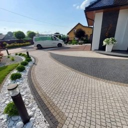 PRAMIX Mariusz Połeć - Zakrzywiony chodnik z kostki brukowej w odcieniach szarości i beżu, obok rabata z białymi kamieniami i niskimi krzewami, w tle dom jednorodzinny oraz firmowy samochód dostawczy z logo.