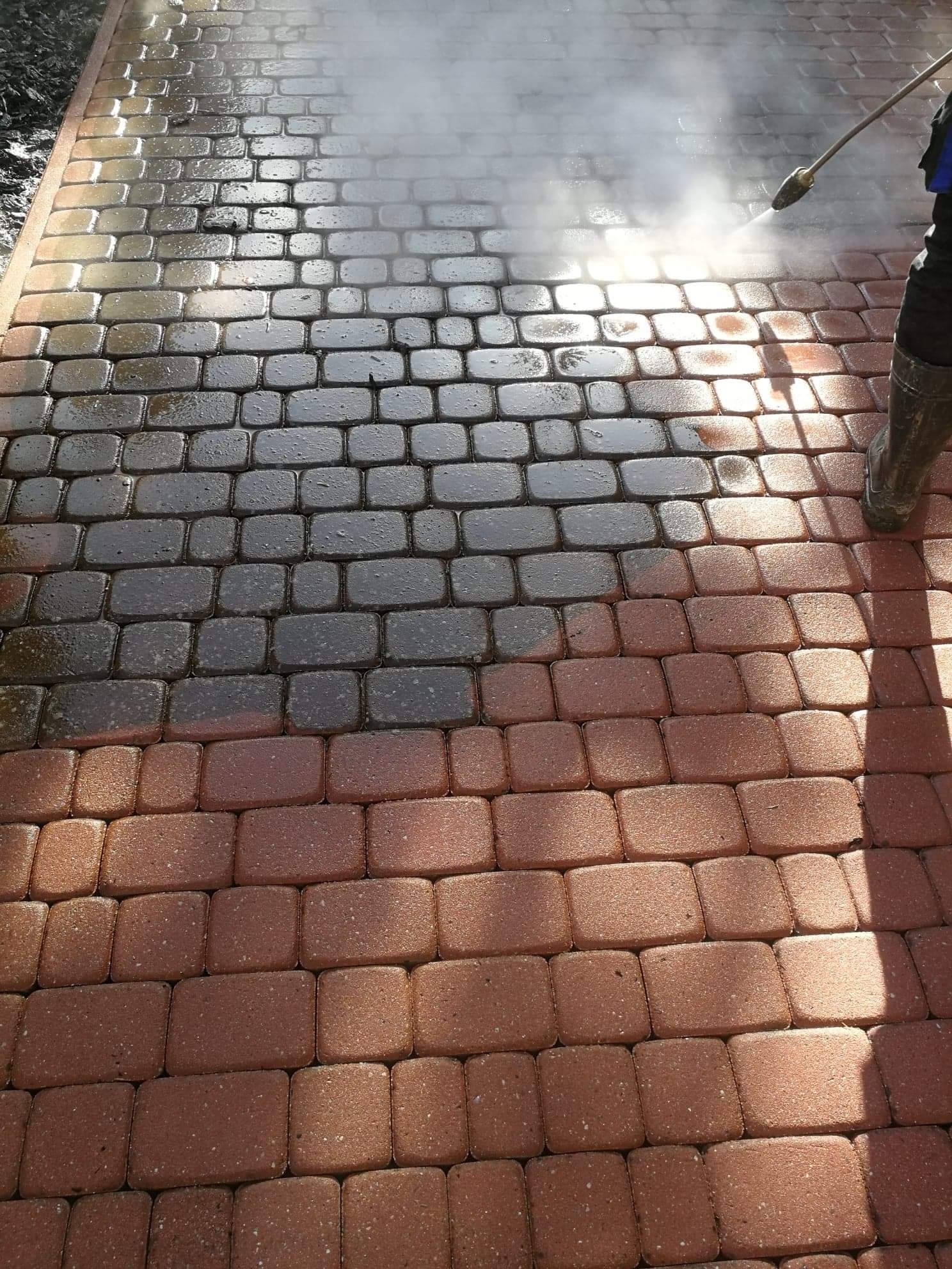 Częściowo wyczyszczona kostka brukowa z czerwonej cegły, myta pod ciśnieniem, z widoczną różnicą między brudną a czystą powierzchnią.
