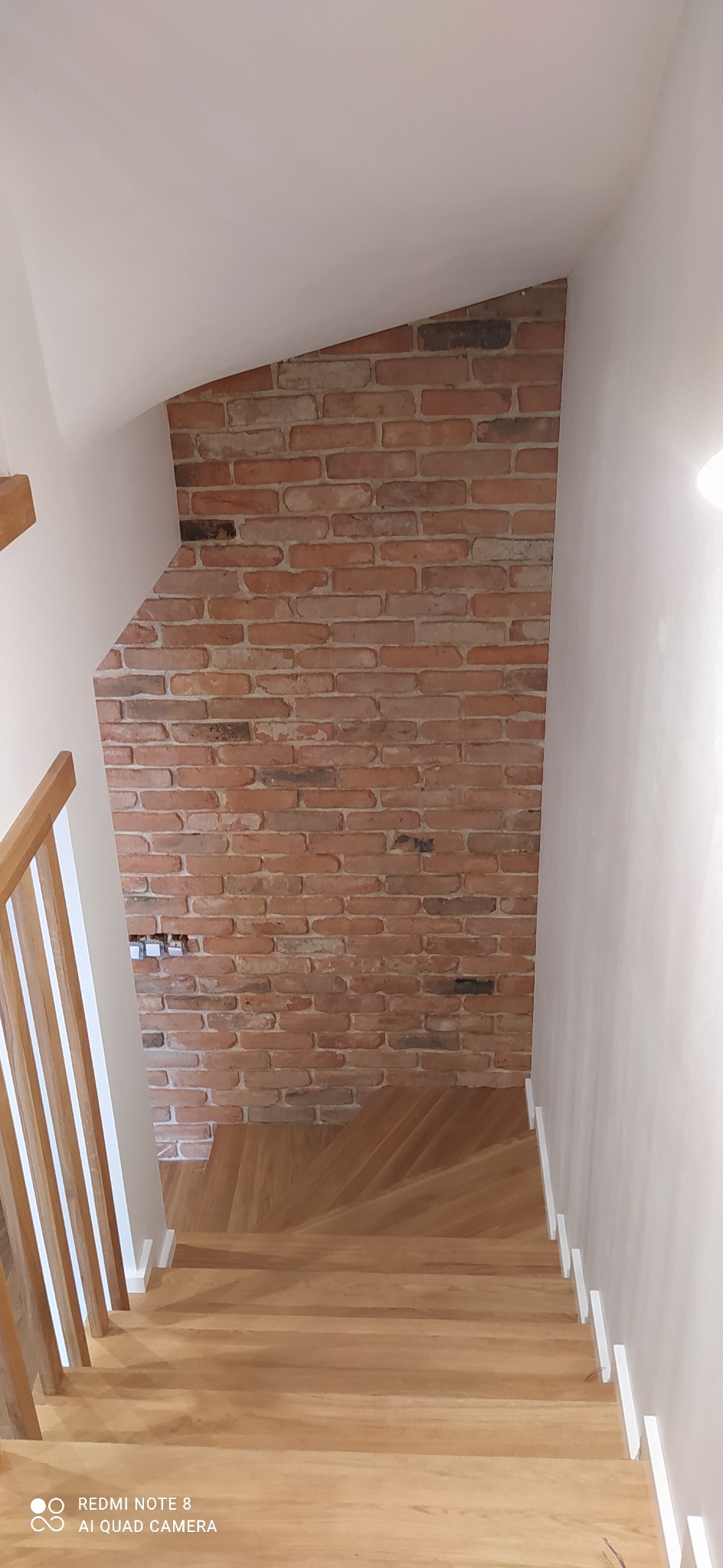 Klatka schodowa z drewnianymi schodami i ścianą wykończoną czerwoną cegłą, widok z góry.