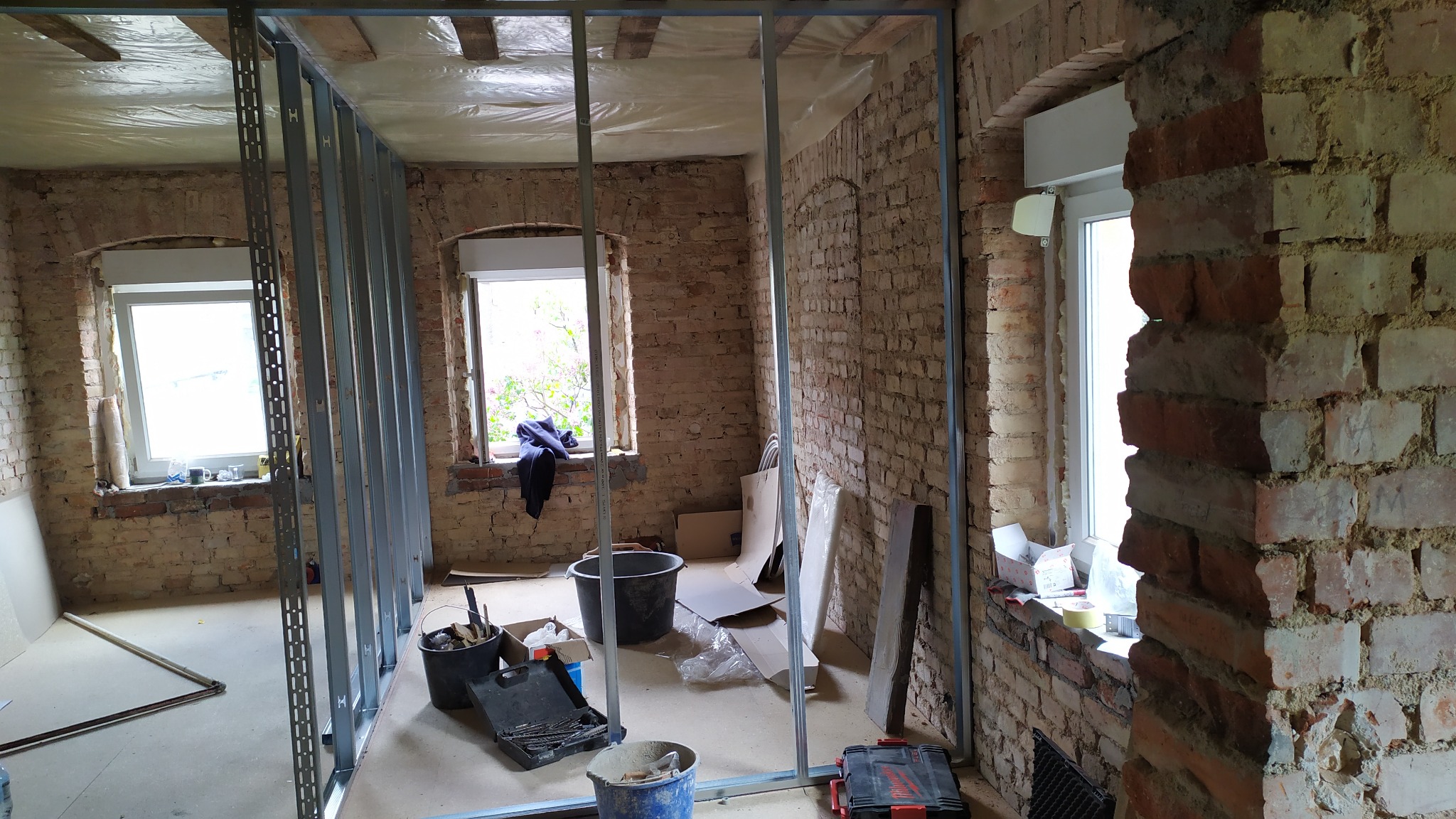 Montaż metalowej konstrukcji pod płytę karton gips na tle surowej ceglanej ściany w remontowanym pomieszczeniu z oknami.