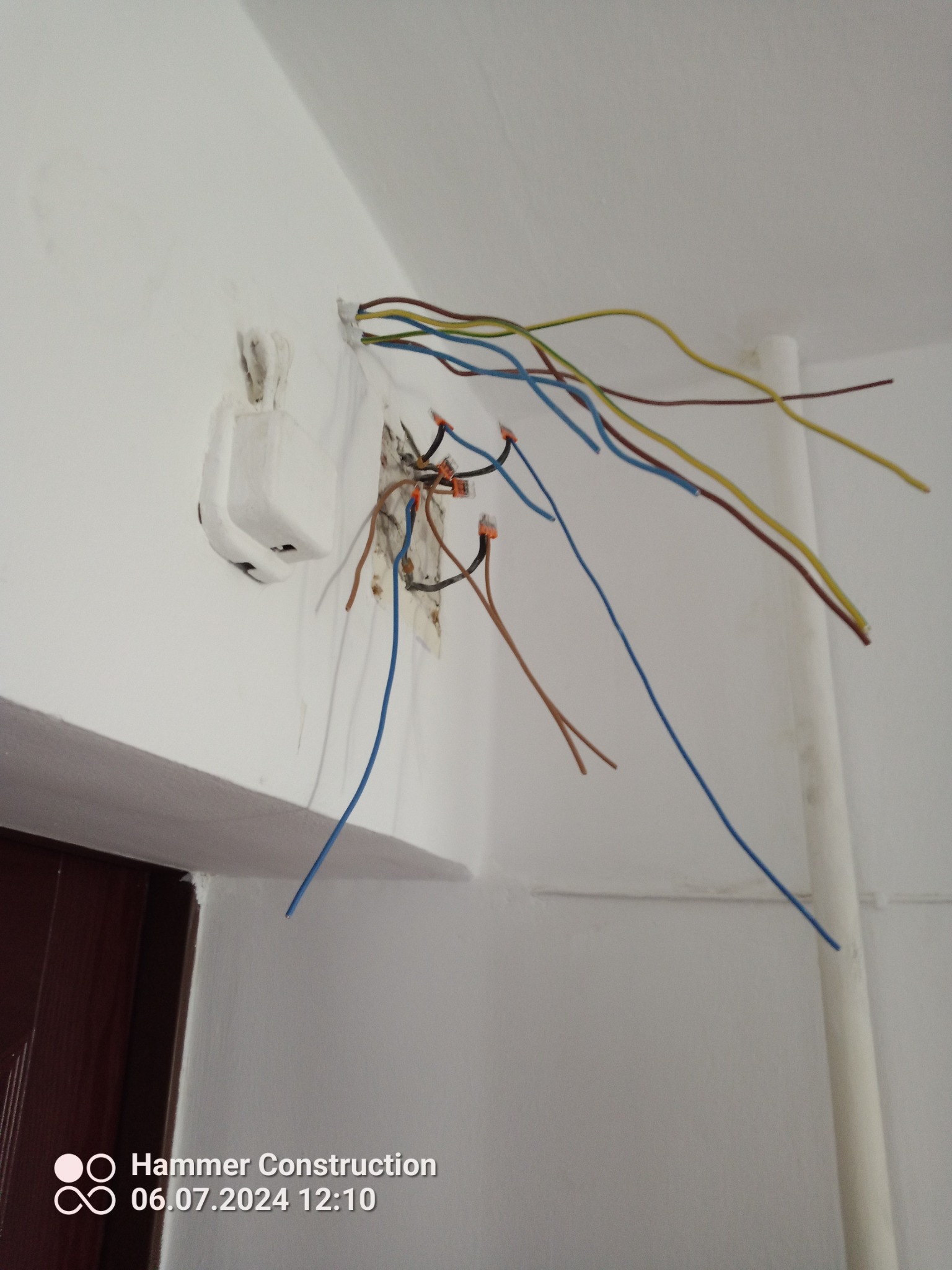 Odsłonięte przewody elektryczne różnej barwy wystające ze ściany obok gniazdka, połączone złączkami WAGO, widoczne ślady po kuciu w ścianie.