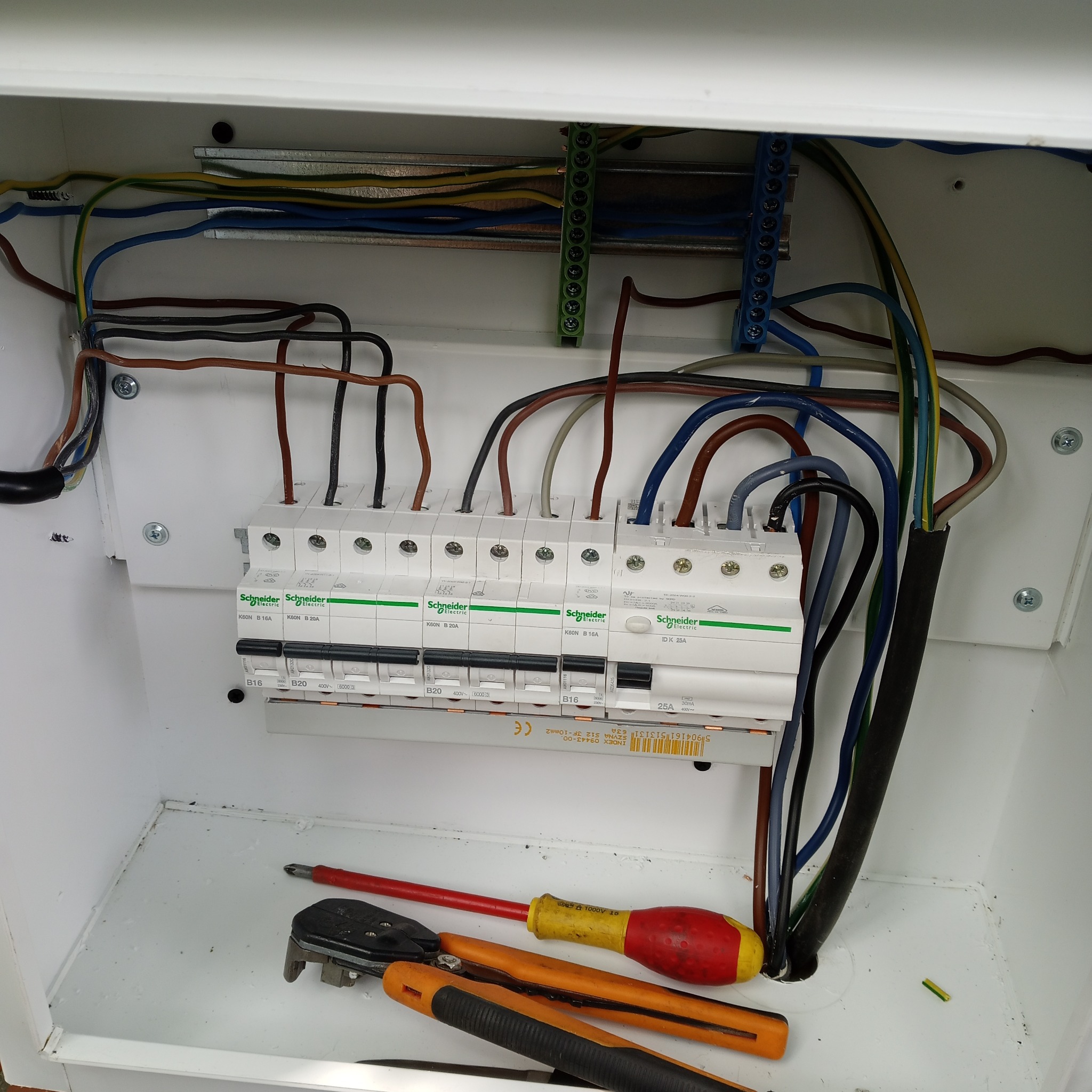 Rozdzielnica elektryczna z zabezpieczeniami różnicowoprądowymi i nadprądowymi marki Schneider Electric w trakcie montażu w Warszawie, widoczne przewody i narzędzia: wkrętak i kombinerki.