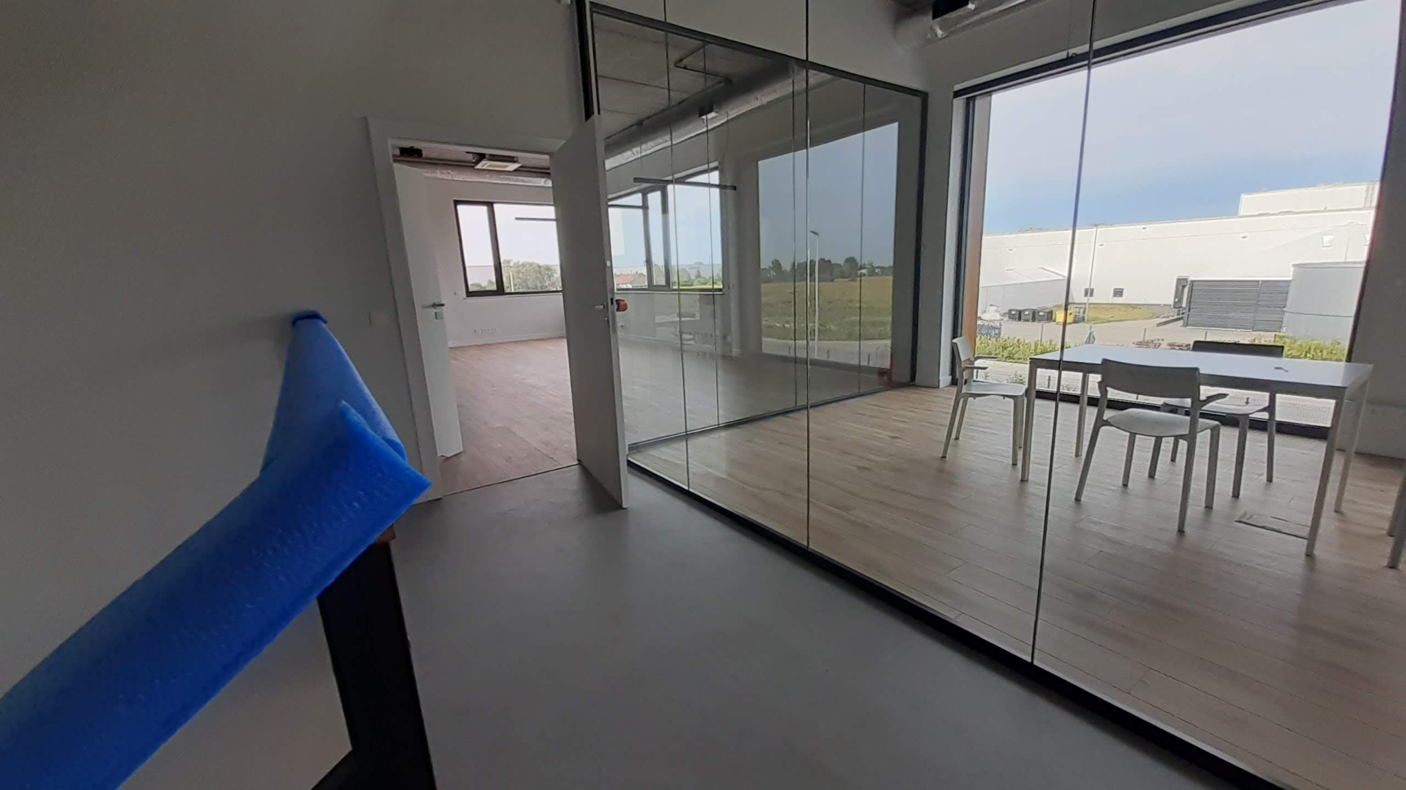 Nowoczesne biuro z przeszkloną salą konferencyjną i widokiem na zewnątrz. Na pierwszym planie zabezpieczenie narożnika ściany. Jasne wnętrze, minimalistyczny design.