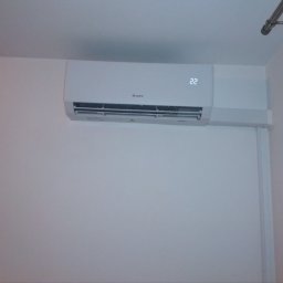 JKB KLIMA KRZYSZTOF BUSZYŃSKI - Biały klimatyzator marki Gree zamontowany na ścianie w pomieszczeniu, wyświetlający temperaturę 22 stopnie Celsjusza.