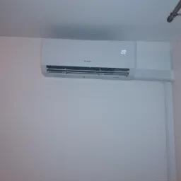 Biały klimatyzator marki Gree zamontowany na ścianie w pomieszczeniu, wyświetlający temperaturę 22 stopnie Celsjusza.