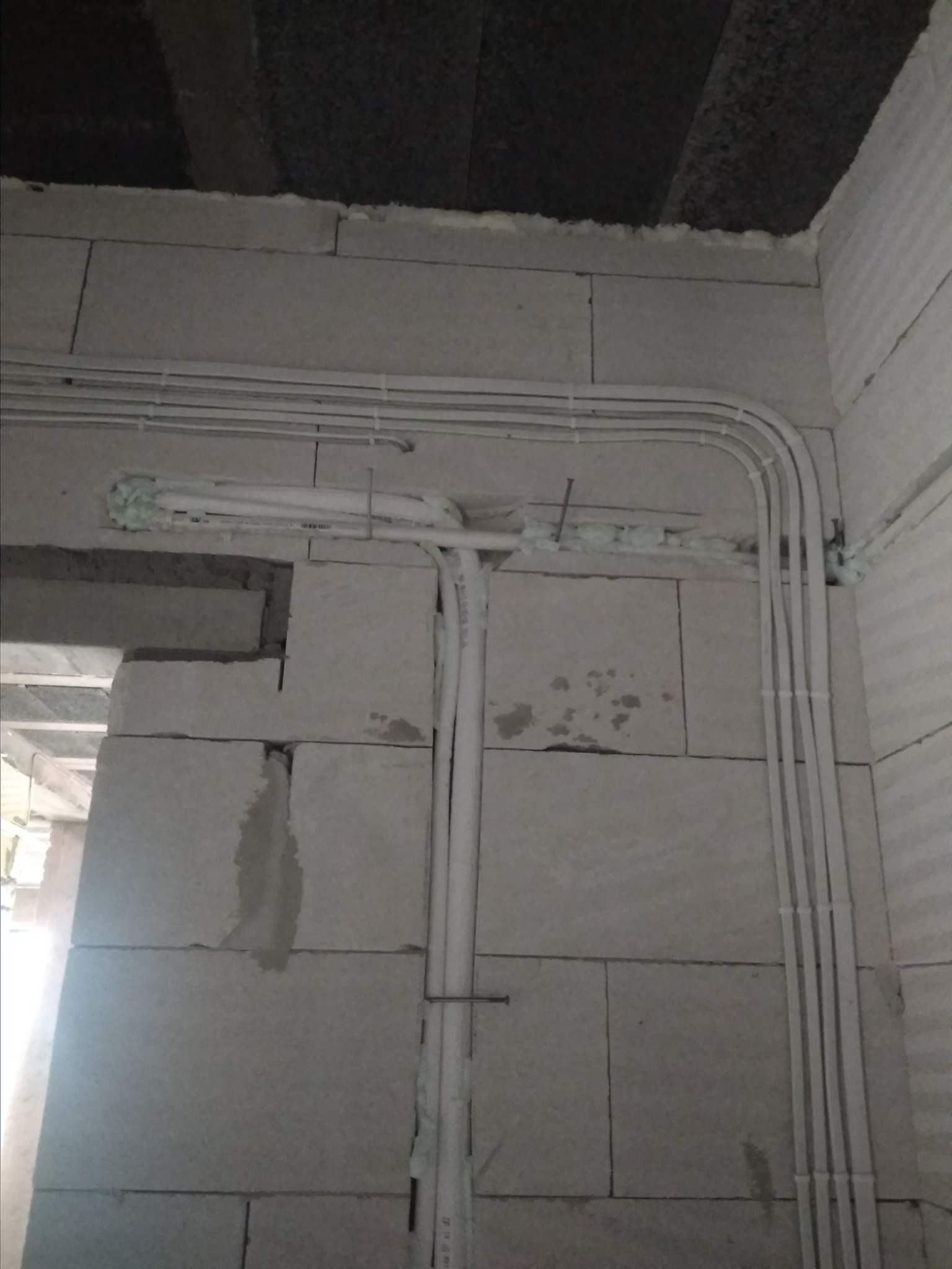 Białe rury wentylacyjne prowadzone po ścianie z betonu komórkowego, zabezpieczone pianką montażową i przymocowane do ściany klamrami i gwoździami.