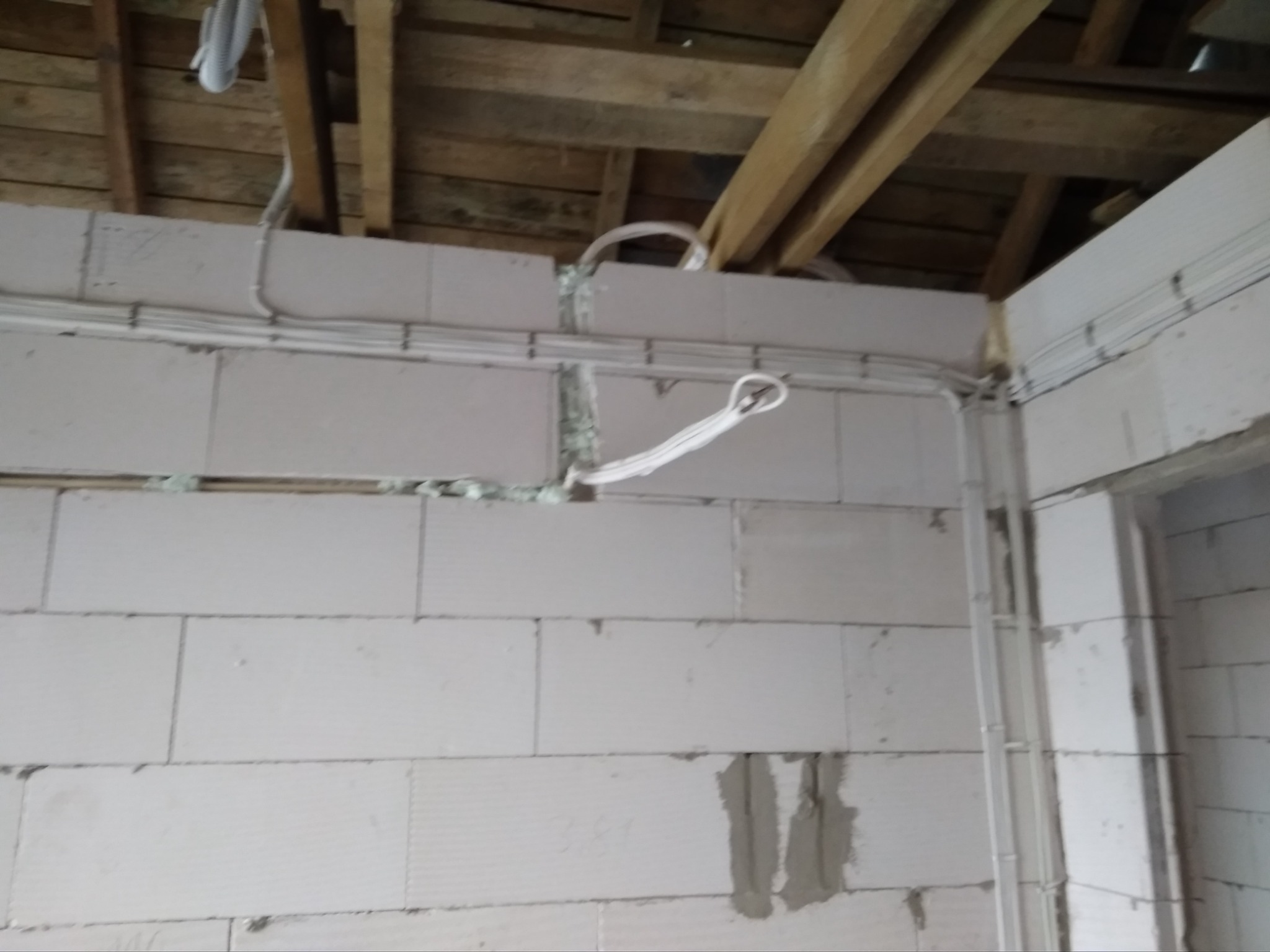 Montaż instalacji wentylacyjnej: białe przewody wentylacyjne prowadzone wzdłuż ściany z betonu komórkowego, widoczne drewniane elementy konstrukcji dachu.