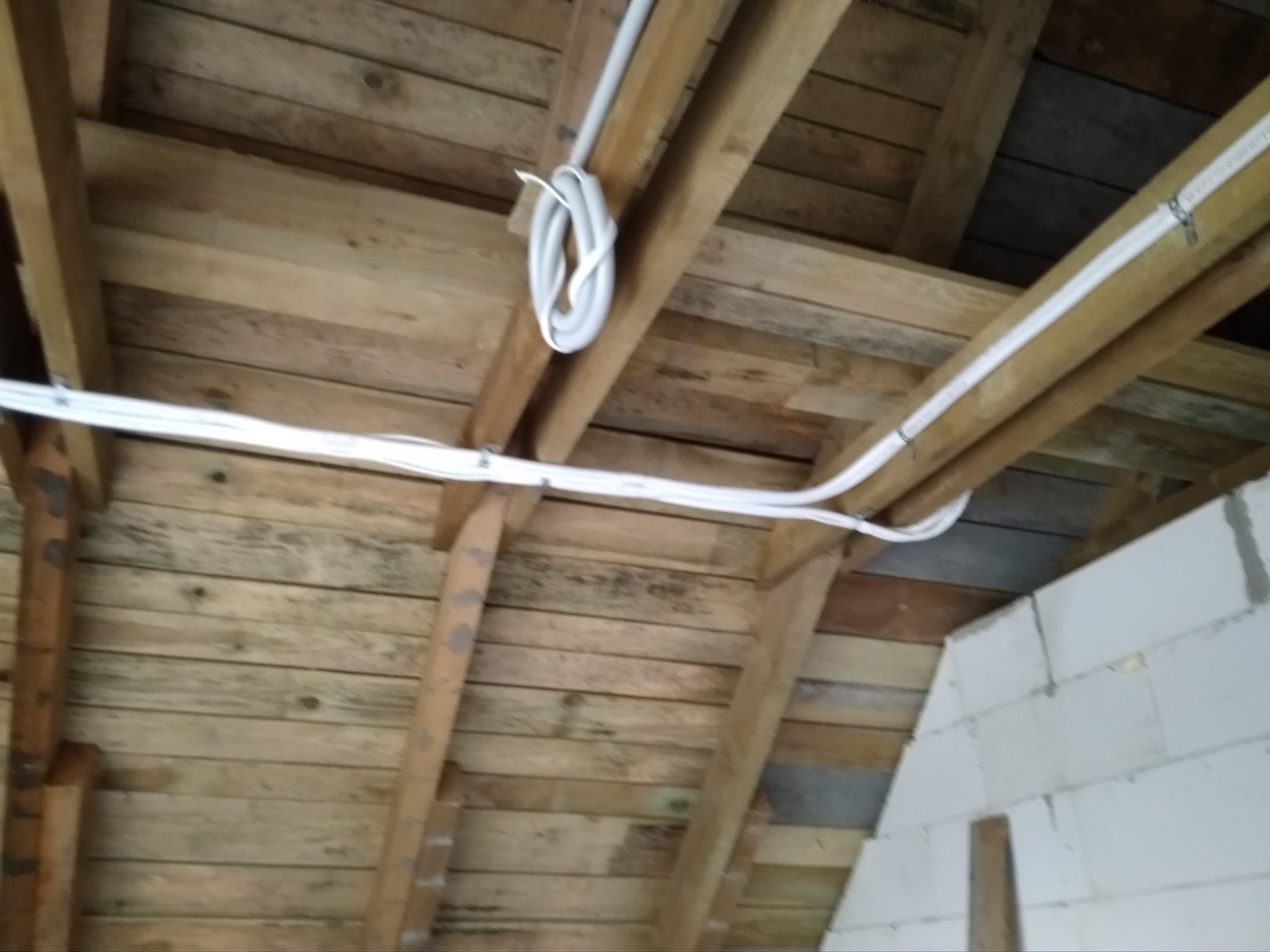 Białe przewody wentylacyjne przymocowane do drewnianej konstrukcji dachu na poddaszu budynku w trakcie budowy.