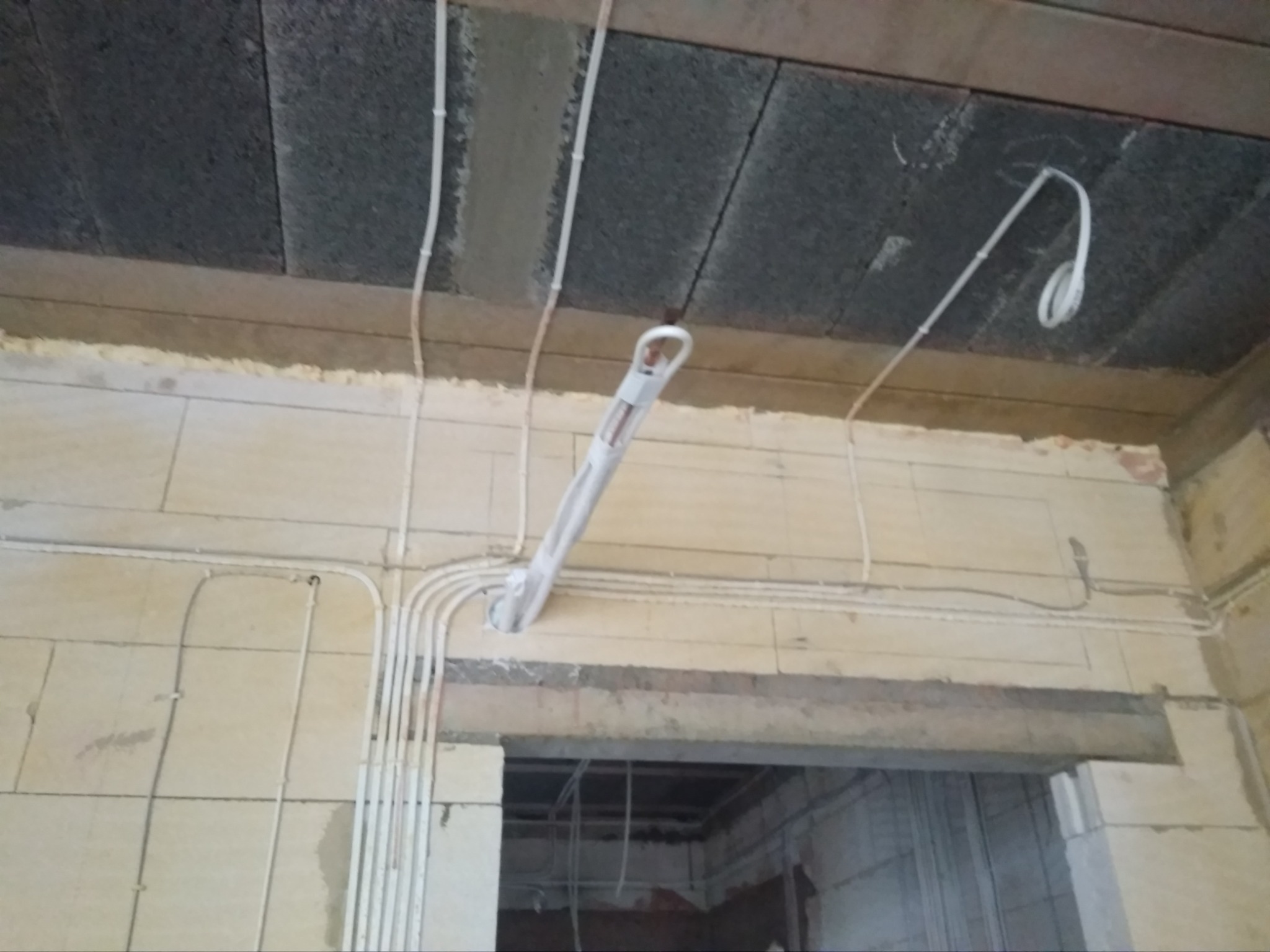 Niedokończona instalacja przewodów wentylacyjnych w surowym wnętrzu budynku z widocznymi blokami betonowymi i otworami na przewody.