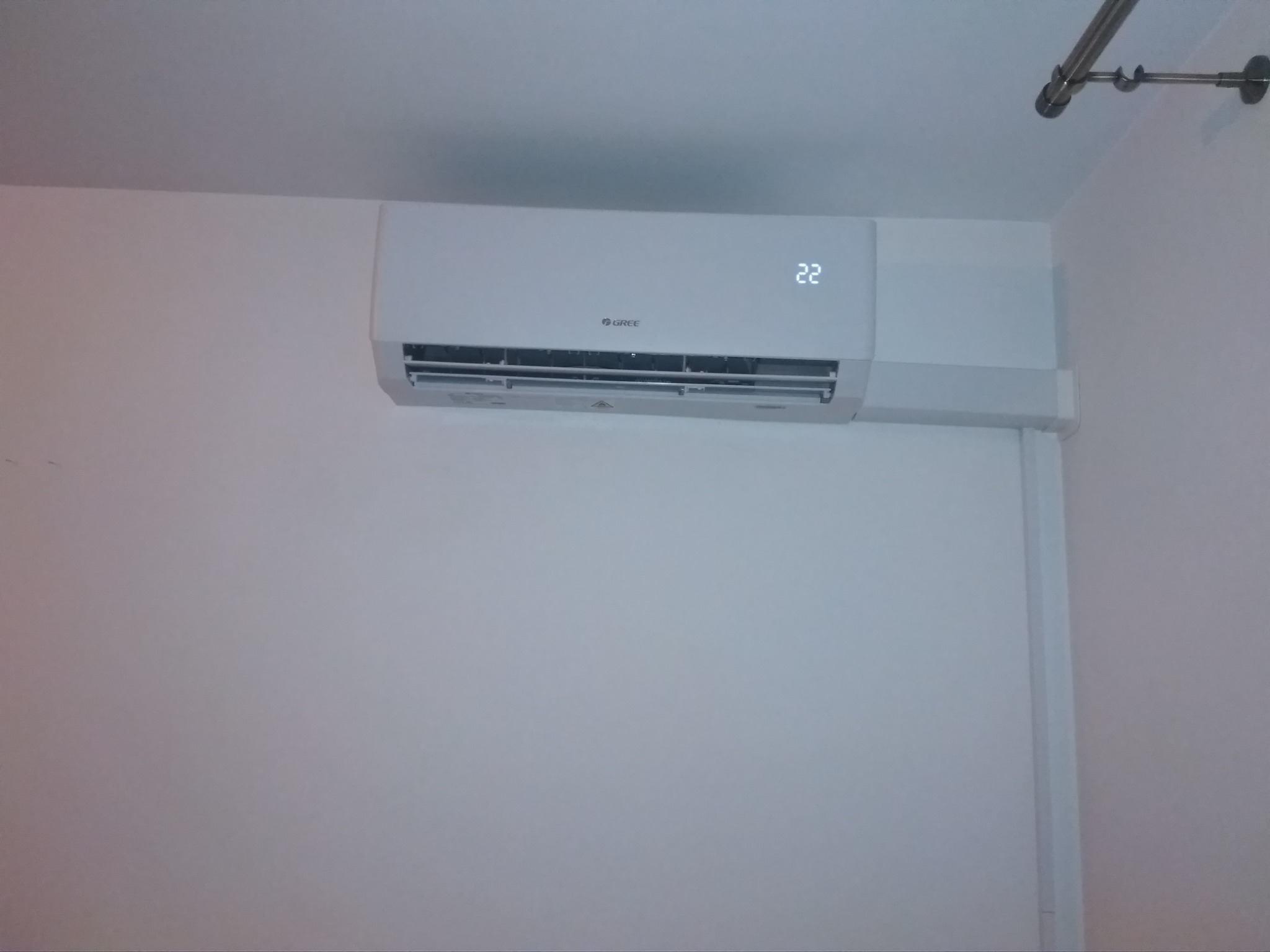 Biały klimatyzator marki Gree zamontowany na ścianie w pomieszczeniu, wyświetlający temperaturę 22 stopnie Celsjusza.