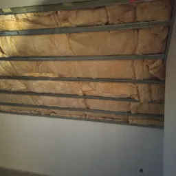 Montaż izolacji z wełny mineralnej w metalowym stelażu pod płytę gipsową, widoczne niedociągnięcia w ułożeniu wełny.