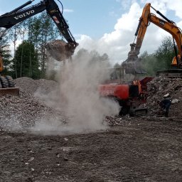 FHU ROLKOP Sebastian Wojciechowski - Dwa żółte i czarne koparki Volvo i JCB pracują przy kruszarce do gruzu na placu budowy, unosząc tumany kurzu, w tle widoczny pracownik w ciemnym ubraniu.