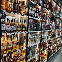 LK Polska Sp. z o. o. - Półki w sklepie z szerokim wyborem butelek alkoholi, w tym whisky, bourbon, wódki i likiery, z cenami na półkach.