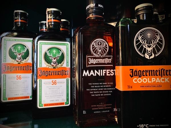 Kilka butelek Jägermeister różnych edycji (Manifest, Coolpack, 56 Botanicals) ustawionych obok siebie, z widocznymi etykietami i logotypem jelenia z krzyżem.