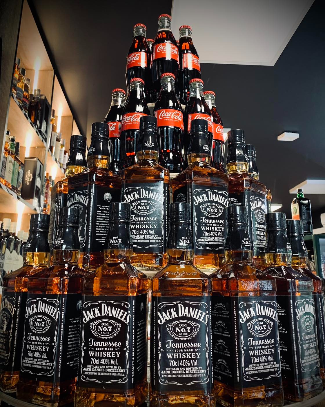 Piramida ułożona z butelek whisky Jack Daniel's i Coca-Coli, ustawiona na barze w sklepie z alkoholami.