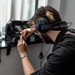 Mężczyzna w słuchawkach PreSonus HD7 podłącza sprzęt audio w torbie obok okna.