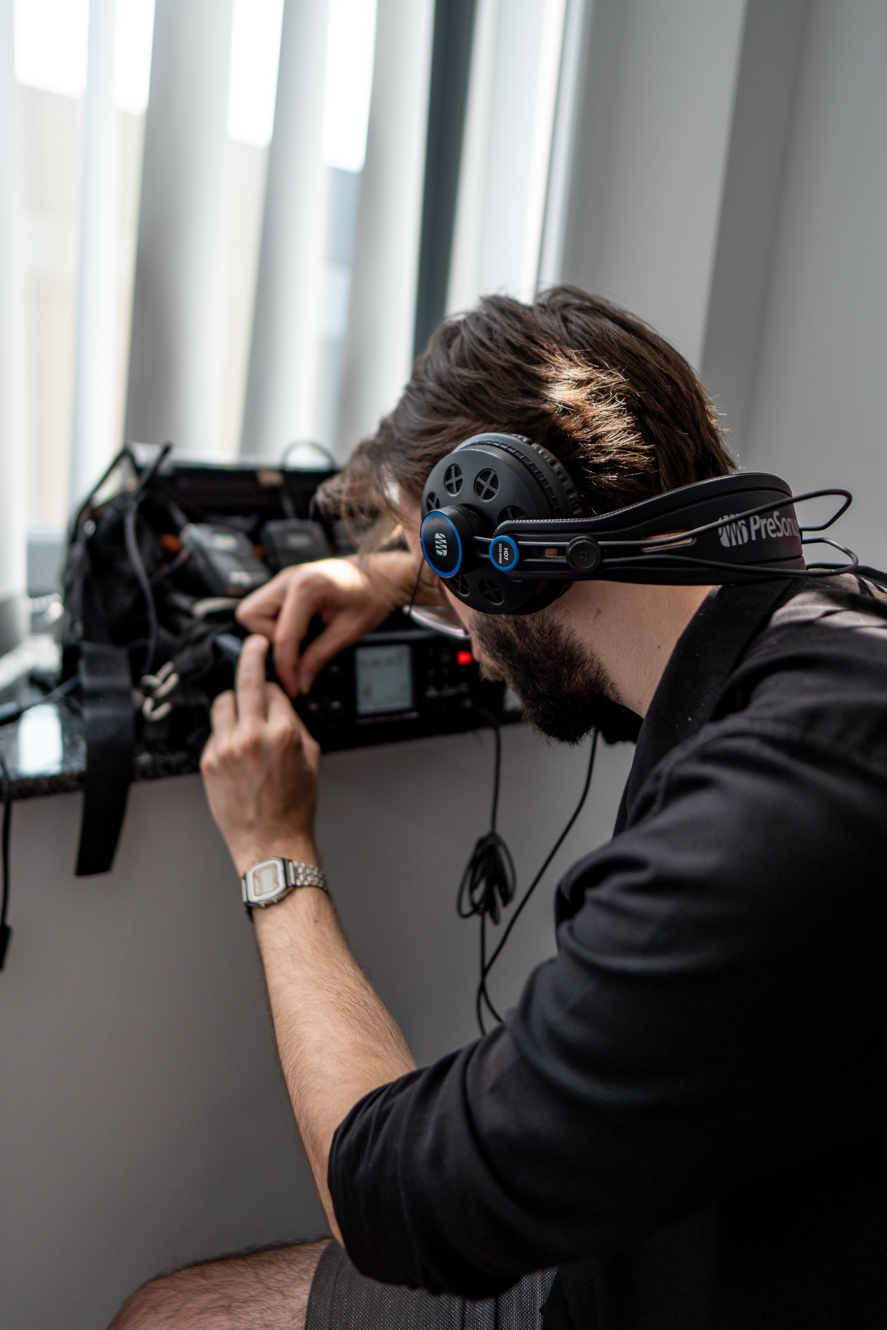 Mężczyzna w słuchawkach PreSonus HD7 podłącza sprzęt audio w torbie obok okna.