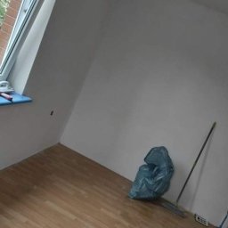 Sam-Bud - Pokój po świeżym malowaniu, z widoczną torbą na śmieci, miotłą i drobnymi zabrudzeniami na podłodze z paneli, okno dachowe po lewej stronie.