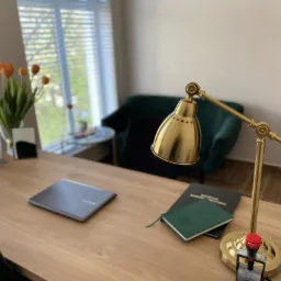 Biuro: drewniane biurko z laptopem, kalendarzem adwokackim 2022, kwiatami w wazonie i złotą lampką biurkową z pieczątką na podstawie