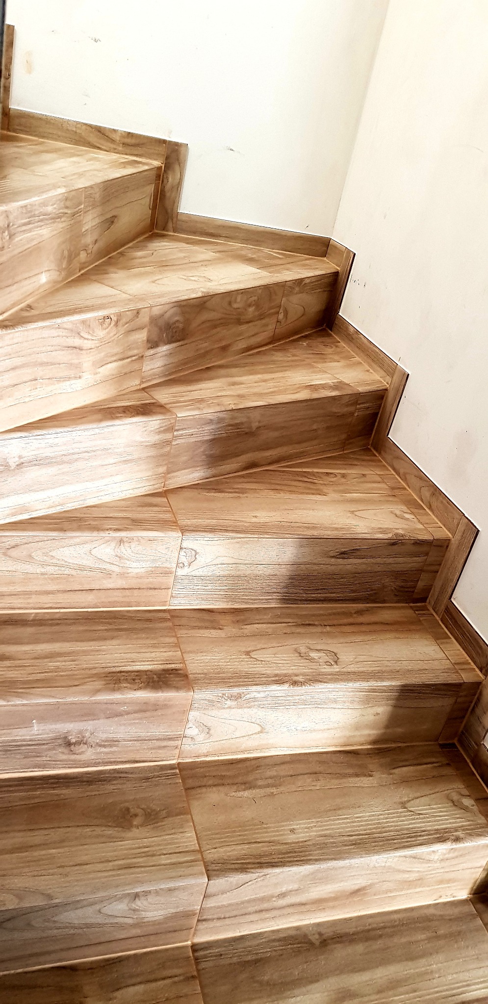 Wyłożone drewnopodobnymi płytkami schody wewnętrzne, widok z dołu na górę, z bliska, fuga w kolorze płytek.