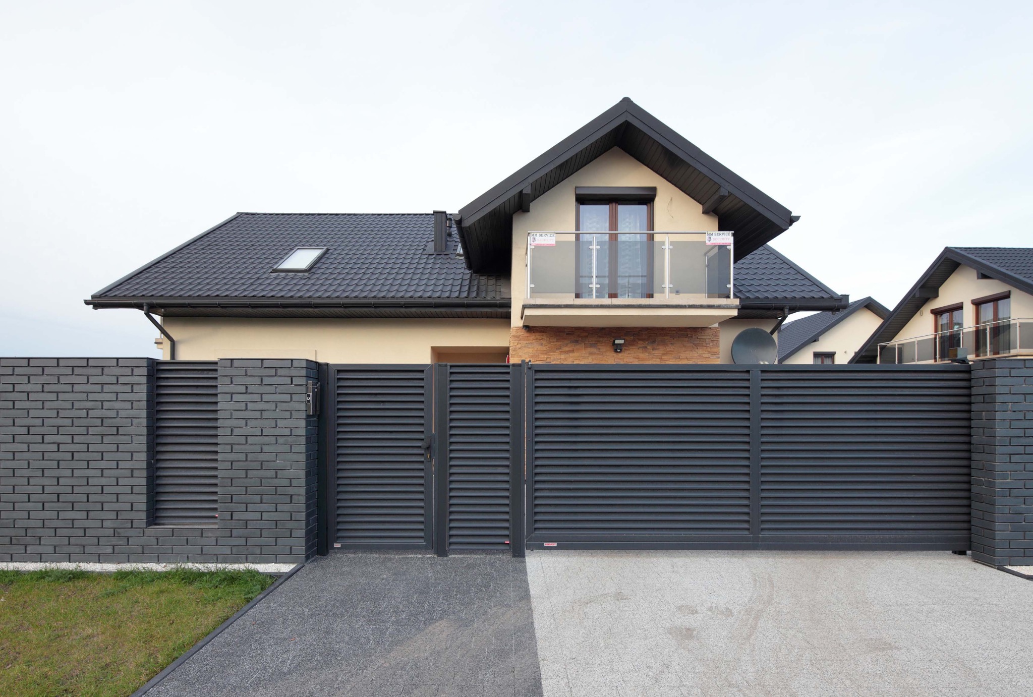 Nowoczesna posesja z grafitowym ogrodzeniem lamelowym i bramą przesuwną, w tle dom z balkonem z balustradą szklaną.