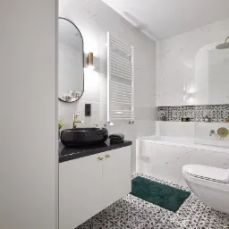 Nowoczesna łazienka z marmurowymi płytkami, czarną umywalką nablatową, złotą armaturą i dekoracyjną podłogą w stylu vintage.