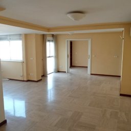 Green & Clean - Puste, jasne wnętrze mieszkania z marmurową podłogą i beżowymi ścianami. Widoczne okna, drzwi i klimatyzator. Gotowe do sprzątania lub remontu.