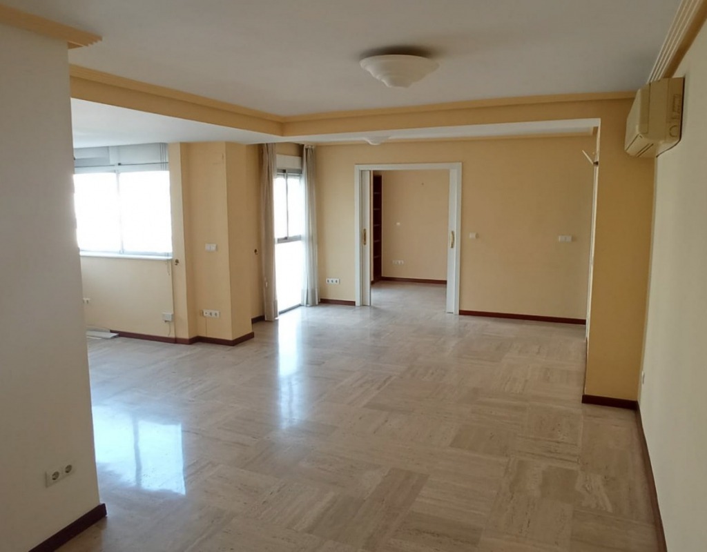 Puste, jasne wnętrze mieszkania z marmurową podłogą i beżowymi ścianami. Widoczne okna, drzwi i klimatyzator. Gotowe do sprzątania lub remontu.