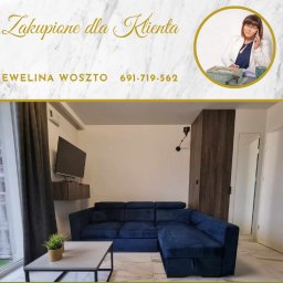 Dzieciogród Ewelina Woszto - Nowoczesny salon z narożnikiem w odcieniach granatu, widok z okna na apartamentowiec. U góry logo z wizerunkiem agentki i napisem 'Zakupione dla Klienta'.