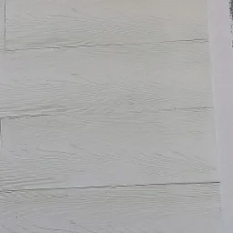 Szczegółowe ujęcie białych paneli elewacyjnych z widoczną strukturą drewna i fragmentem styropianu, ukazujące wykończenie elewacji.