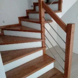 Nowoczesne schody z drewnianymi stopniami i białymi podstopnicami oraz balustradą z drewnianych słupków i metalowych prętów.