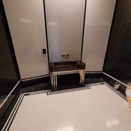 Seb- Bud - Nowoczesna łazienka z umywalką na postumencie z ciemnego drewna i złotymi akcentami, białe ściany z czarnymi obramowaniami, podłoga z białych płytek z czarnymi i białymi bordiurami, minimalistyczny...