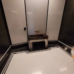 Nowoczesna łazienka z umywalką na postumencie z ciemnego drewna i złotymi akcentami, białe ściany z czarnymi obramowaniami, podłoga z białych płytek z czarnymi i białymi bordiurami, minimalistyczny...