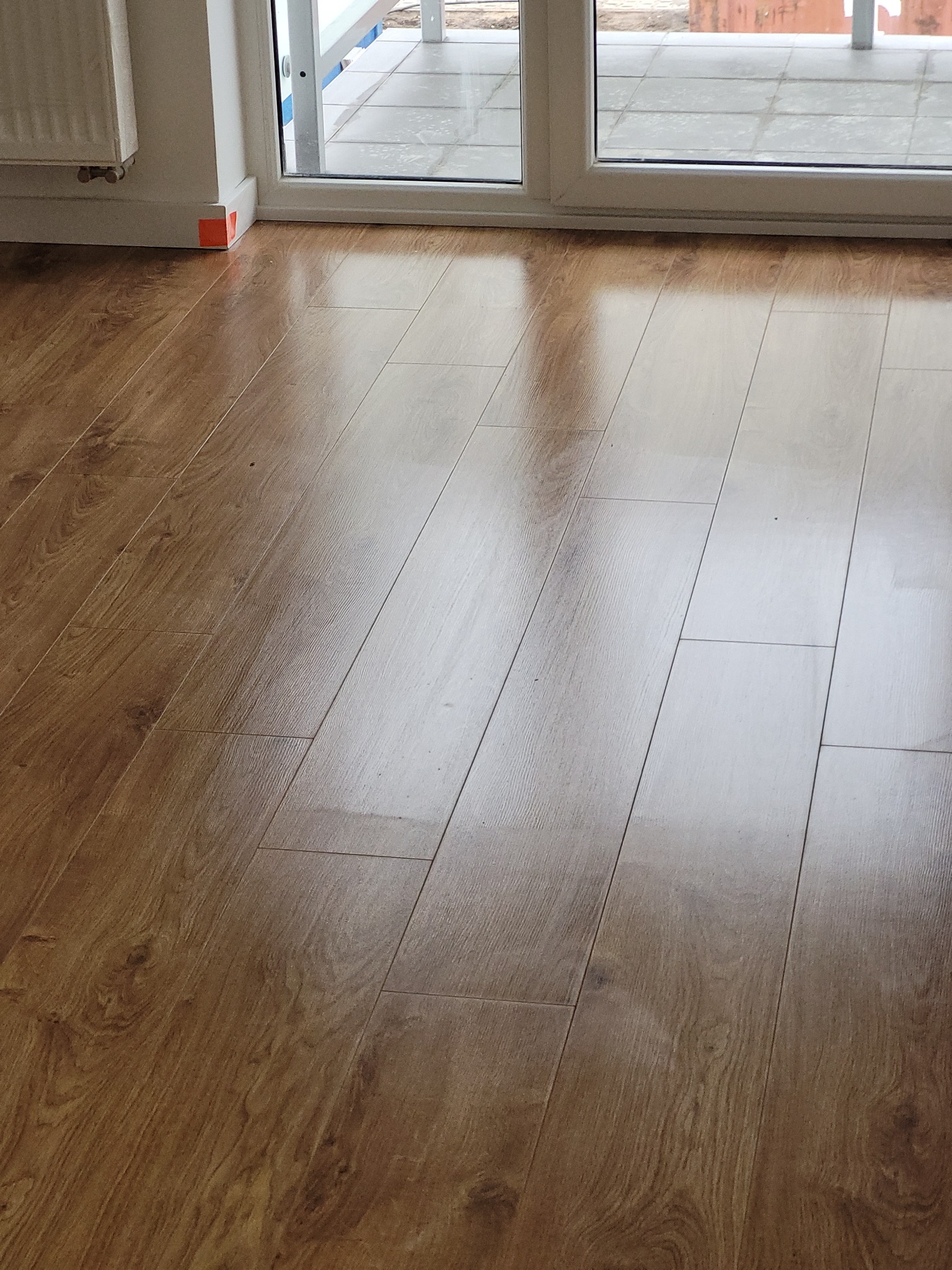 Ułożone panele podłogowe w odcieniach brązu, widoczne przy białych drzwiach balkonowych w mieszkaniu w Poznaniu.