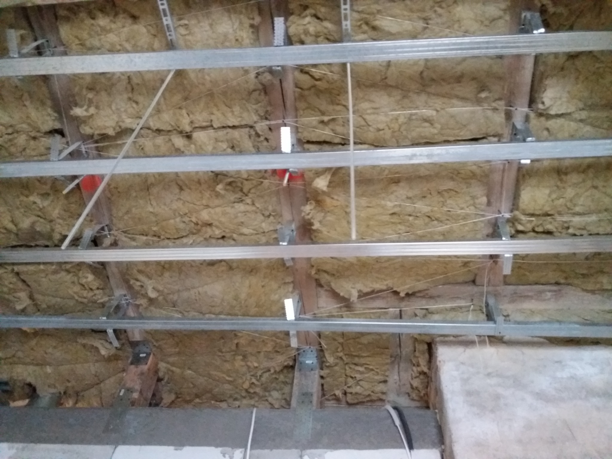 Izolacja poddasza wełną mineralną między krokwiami z zamontowanym stelażem metalowym do podwieszanego sufitu.