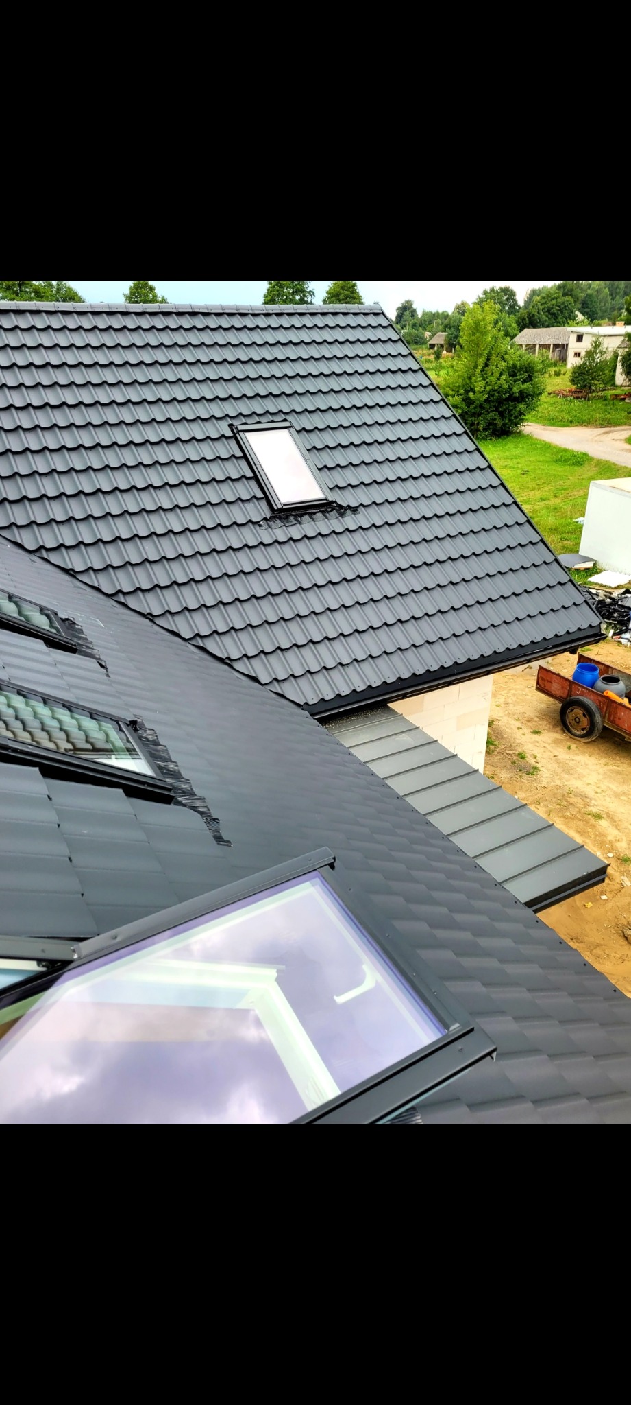 Nowy, grafitowy dach z dachówki modułowej z oknami połaciowymi, widok z góry na budynek w trakcie budowy.