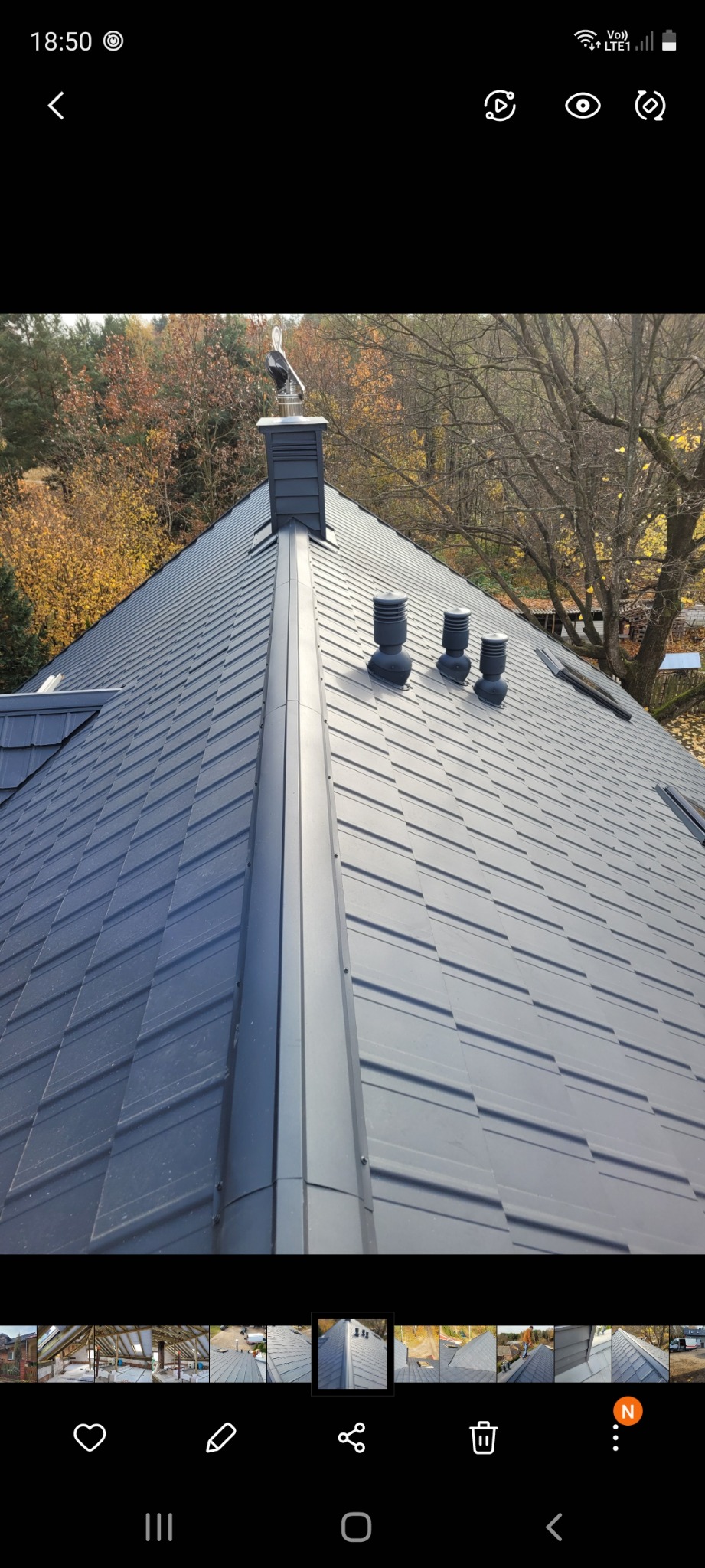 Nowy, grafitowy dach z blachy trapezowej z kominem i trzema odpowietrznikami, widok z góry na tle jesiennego lasu.