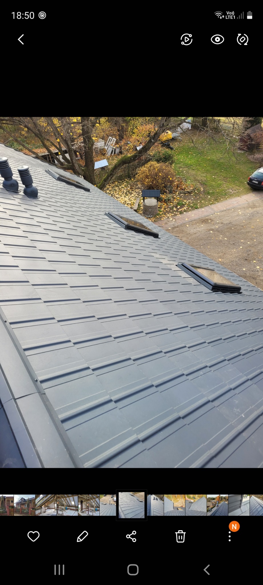 Szary dach z blachy trapezowej z trzema kominkami wentylacyjnymi i dwoma oknami dachowymi, widok z góry na otoczenie z drzewami i studnią