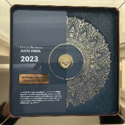 Dyplom w ramce, nagroda 'Złota Firma 2023' dla 'Atut Ubezpieczenia Teresa Stefańska', z motywem ornamentu w kolorze złotym.