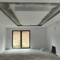 Wnętrze pokoju w trakcie remontu, z częściowo zamontowanym, podwieszanym sufitem z płyt kartonowo-gipsowych, widoczne przygotowania do wykończenia i pomalowania ścian.