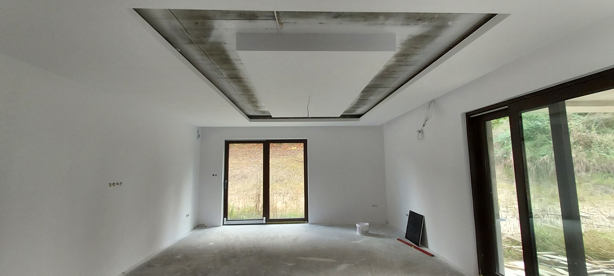 Wnętrze pokoju w trakcie remontu, z częściowo zamontowanym, podwieszanym sufitem z płyt kartonowo-gipsowych, widoczne przygotowania do wykończenia i pomalowania ścian.