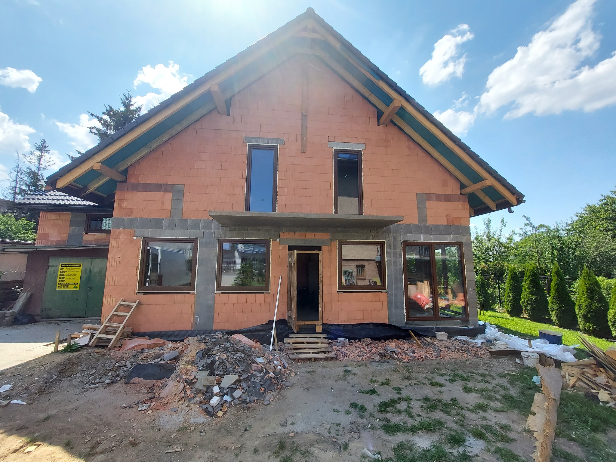 Dom w stanie surowym otwartym z zamontowanymi oknami i przygotowanym wejściem, widoczne materiały budowlane i rusztowanie.